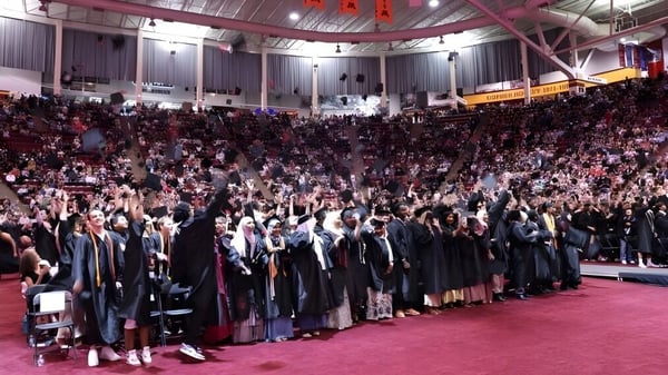 Estudiantes de Eden Prairie Schools se reúnen en sus togas de graduación durante una ceremonia en un gran salón.