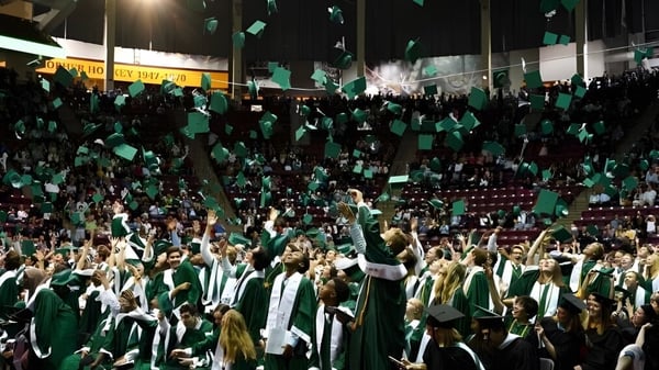 Un gran grupo de estudiantes de Edina Public Schools lleva togas y sombreros verdes en una celebración en el estadio.