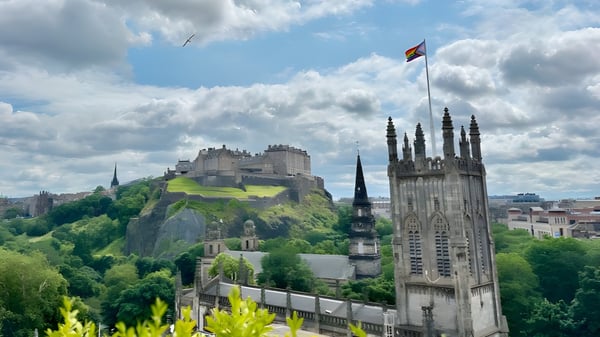 El edificio de la Edinburgh Steiner School se encuentra en una colina rocosa con una catedral al fondo y una bandera en el cielo.