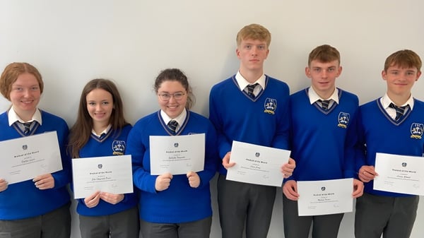 Alumnos del Edmund Rice College en uniformes escolares sosteniendo certificados frente a un fondo blanco.