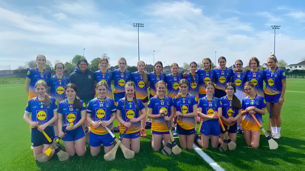 Un grupo de atletas femeninas posando en el campo deportivo del Edmund Rice College con luces de estadio de fondo.