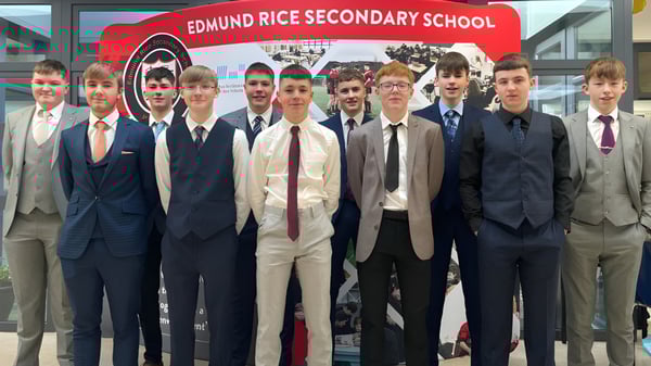 Un grupo de estudiantes está vestido de forma formal frente a un cartel de la Edmund Rice Secondary School.