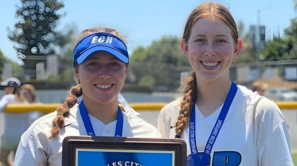 Dos estudiantes sonrientes de la El Camino Real Charter High School están frente a un cuerpo de agua con árboles y edificios al fondo.