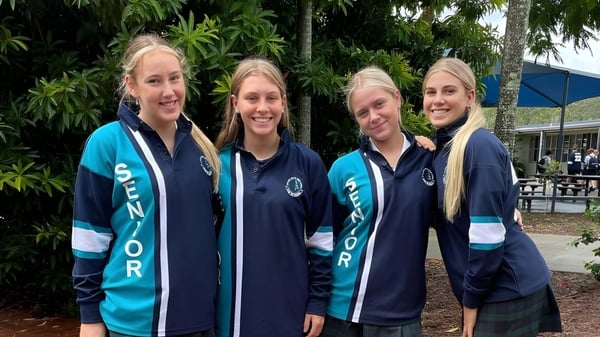 Cuatro estudiantes de Elanora State High School están en el área exterior tropical con palmeras de fondo.