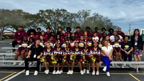 Un grupo de animadoras en uniformes color burdeos posan juntas en el campo deportivo de la Elite Preparatory Academy.