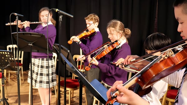 Un grupo de músicos en trajes morados toca en el escenario del Ellesmere College diferentes instrumentos como violines y batería.