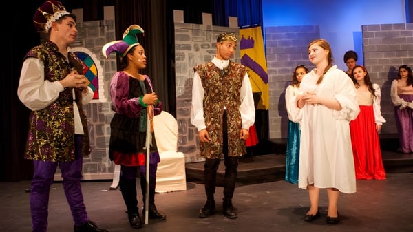 Estudiantes de la Elphinstone Secondary School están en coloridos trajes en un escenario frente a una pared de piedra.