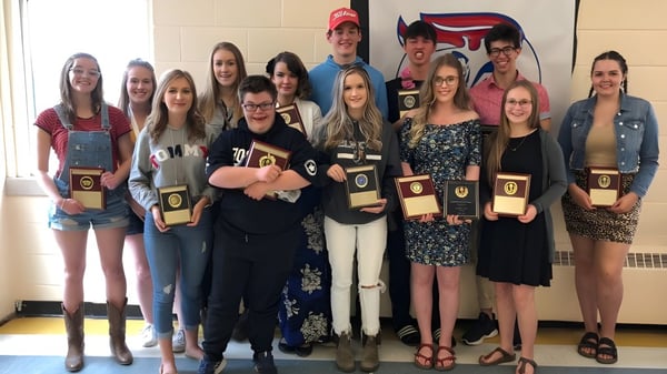 Un grupo de estudiantes de Elwood Regional High posan juntos con trofeos en un entorno escolar.