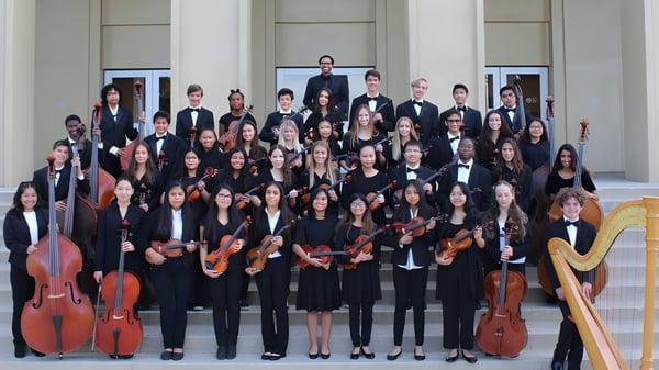 Un gran grupo de músicos en ropa formal está de pie frente a un edificio de diseño clásico en el campus de la Embley.