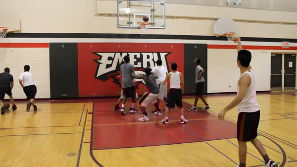 Un grupo de estudiantes juega baloncesto en la cancha del Emery Collegiate Institute frente a una gran publicidad de Exert.