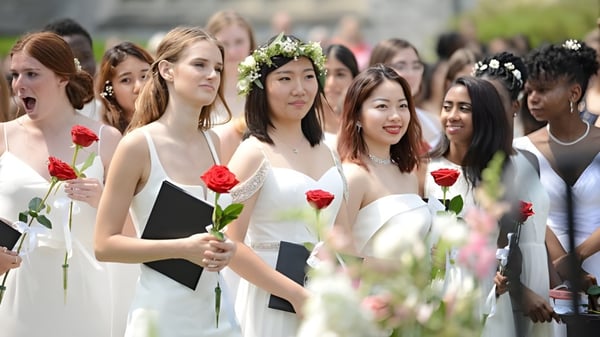 Un grupo de jóvenes estudiantes de la Emma Willard School está al aire libre con rosas rojas frente a edificios y áreas verdes.