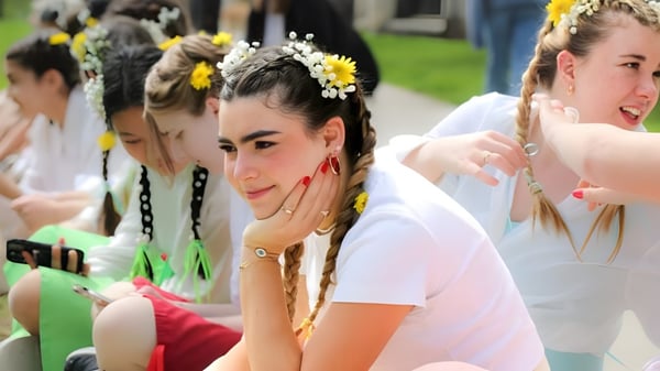Un grupo de jóvenes mujeres con vestidos blancos y coronas de flores está en un campo en el campus de la Emma Willard School.