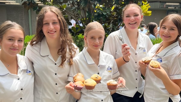 Estudiantes de la Engadine High School muestran una bandeja con productos de panadería recién horneados frente a un fondo verde.