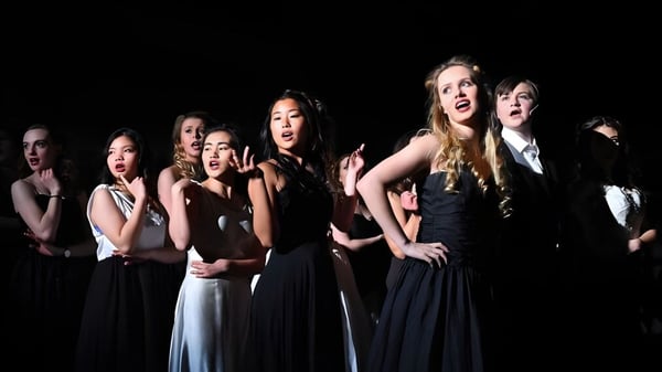 Un grupo de estudiantes de Epsom College presenta una obra de teatro en un escenario iluminado tenuemente.