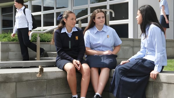 Un grupo de alumnas de la Epsom Girls Grammar School está sentada en los escalones del edificio escolar y conversan.