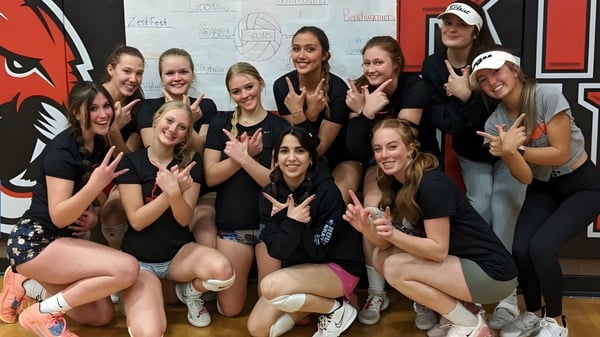 Un grupo de jóvenes mujeres con camisetas negras posan juntas frente a una pared con gráficos en el campus de Erie High School.