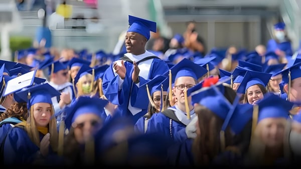 Un gran grupo de graduadas y graduados en togas azules está reunido frente a la Erin District High School.