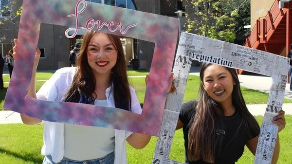 Dos estudiantes de la Escondido Charter High School sostienen un gran marco en forma de corazón en un prado frente al edificio escolar.