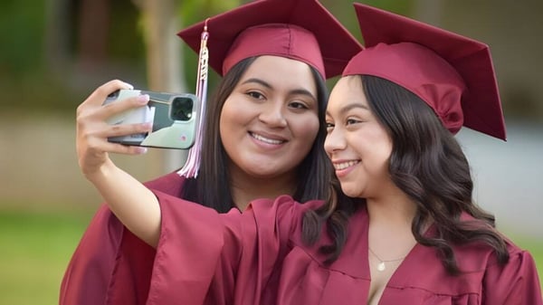 Dos estudiantes en ropa de graduación de la Escondido Charter High School se toman un selfie juntas al aire libre.