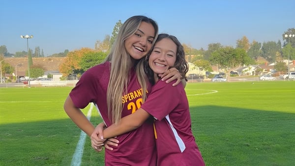 Dos estudiantes en camisetas rojas se abrazan en un campo en el campus de la Esperanza High School.