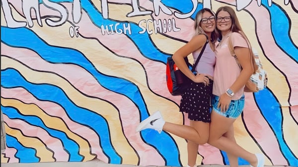 Dos estudiantes posan frente a un colorido mural con la inscripción High School en la Esperanza High School.