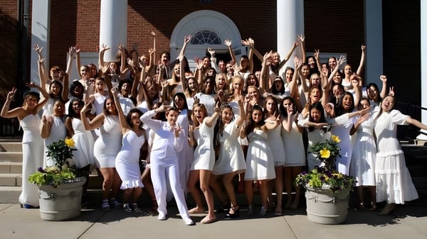 Estudiantes de la Ethel Walker School se reúnen en las escaleras de un edificio de ladrillo y levantan los brazos en pose de celebración.