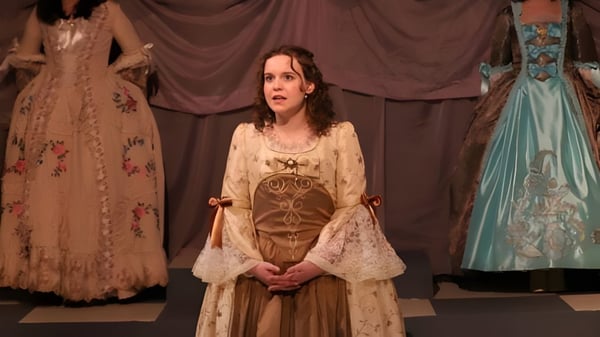 Una mujer con un vestido artísticamente decorado está frente a una cortina en un escenario del Eugene School District.
