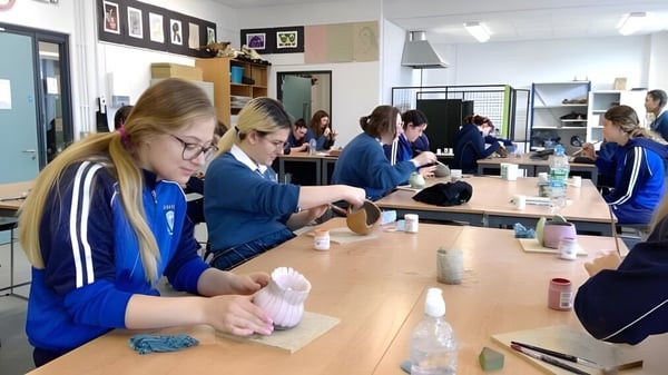 Alumnos de la Eureka Secondary School llevan uniformes azules y organizan materiales en un aula.