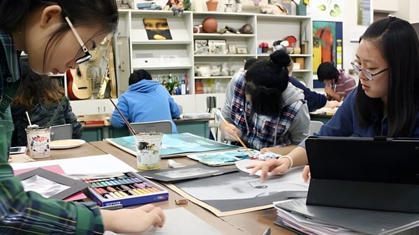 Estudiantes de la Evan Hardy Collegiate trabajan juntos en el estudio de arte con varios utensilios de pintura en el fondo.
