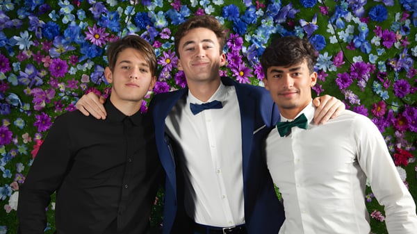 Tres estudiantes del F-1 No Choice Programm USA posan juntos frente a un colorido fondo de flores.