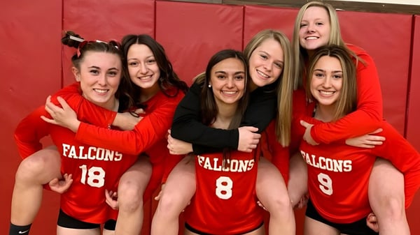 Cinco estudiantes de la Fabius Pompey High School en camisetas deportivas rojas de Falcons posan juntas frente a un fondo rojo.
