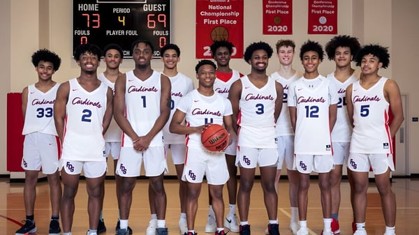Un grupo de jugadores de baloncesto en uniformes blancos con la inscripción Colonials en el gimnasio de la Fairfax Christian School.