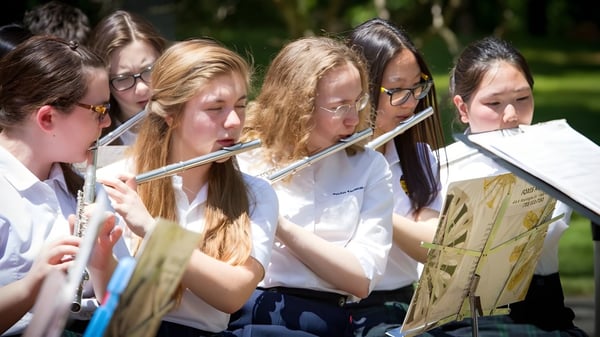 Estudiantes de la Fairfax Christian School tocan instrumentos musicales al aire libre frente a un fondo verde.