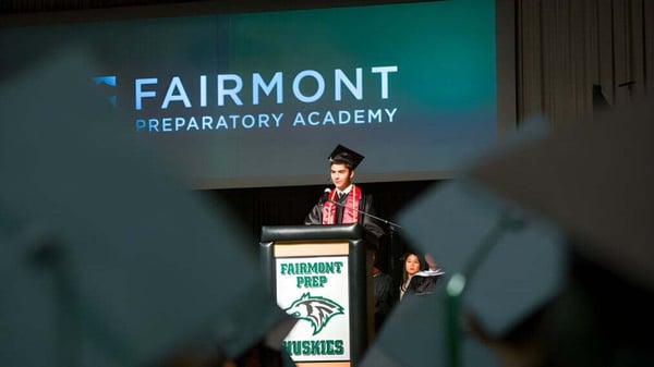 Una persona da un discurso en el podio frente a una pantalla con el logo de Fairmont Prep Academy.