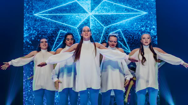 Un grupo de alumnas de la Faith Christian Academy (FL) realiza una actuación de danza en el escenario frente a un fondo geométrico iluminado.