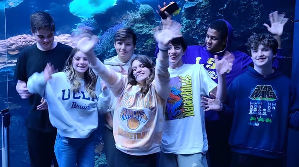 Un grupo de estudiantes de la Faith Christian School posan frente a una imagen submarina con coloridos corales y criaturas marinas.