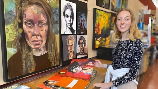 Una mujer está frente a una pared con retratos coloridos y trabaja artísticamente en el campus de la Farlington School.