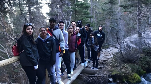 Estudiantes de la Father Lacombe High School caminan por un sendero de madera a través de un área boscosa.