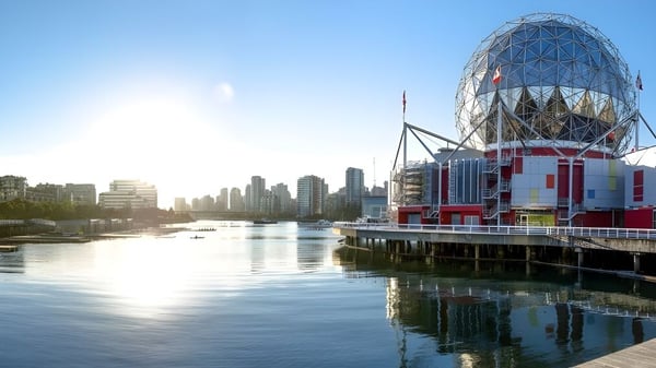 El moderno edificio de la Father Lacombe High School con una construcción de vidrio y acero en forma de huevo se encuentra en un muelle junto a un agua tranquila.