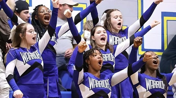 Grupo de animadoras de la Fayetteville Christian School actúan en uniformes morados en un campo deportivo.