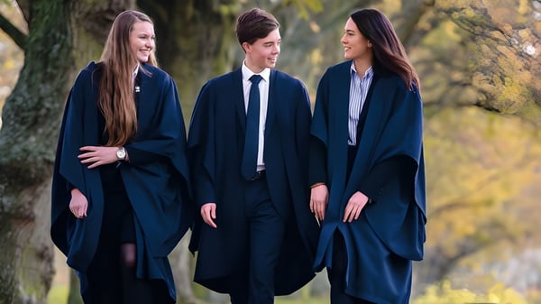 Tres estudiantes de la Felsted School están en el bosque y llevan túnicas académicas oscuras.