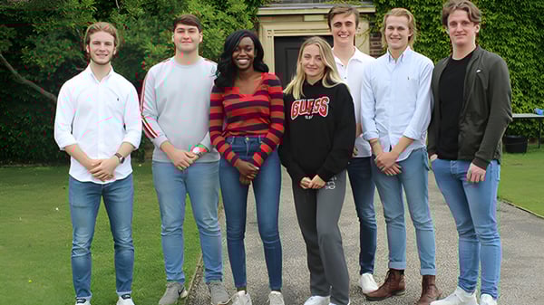 Un grupo de estudiantes está en el terreno de la Felsted School en un prado con árboles y edificios al fondo.