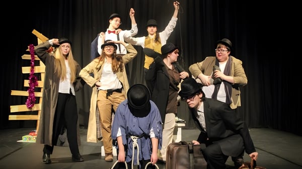 Un grupo de intérpretes en trajes coloridos en el escenario de la Ferndown Upper School durante una actuación.