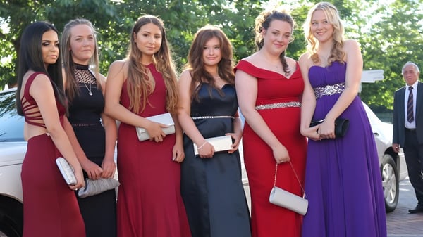 Un grupo de estudiantes de la Ferndown Upper School está de pie en ropa formal frente a un coche ante un fondo verde.