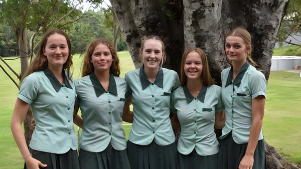 Un grupo de cinco estudiantes de la Ferny Grove State High School está frente a un árbol con densa follaje.