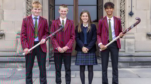 Cuatro personas en ropa formal están de pie frente a un edificio en el campus del Fettes College.