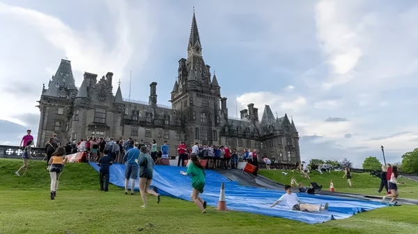 El gran edificio parecido a una catedral del Fettes College se encuentra al fondo sobre un campo de hierba con un grupo de personas.
