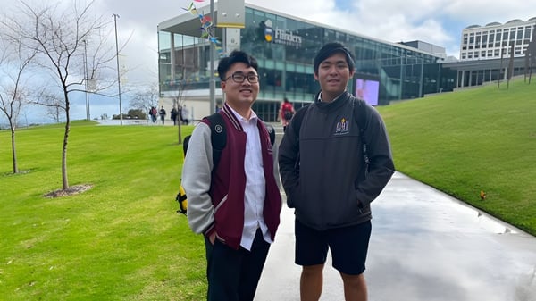 Dos estudiantes están de pie frente a un edificio moderno en el campus de Findon High School con un área de césped al fondo.