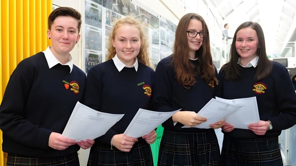 Cuatro estudiantes en el pasillo del Fingal Community College llevan uniformes escolares y sostienen papeles.