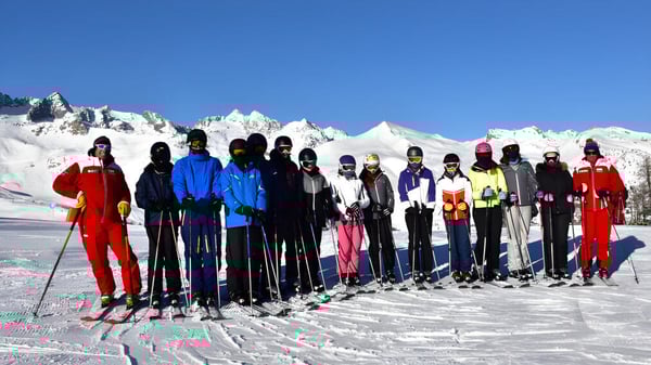 Estudiantes de la Firrhill High School están vestidos de colores en una pendiente cubierta de nieve con montañas nevadas de fondo.